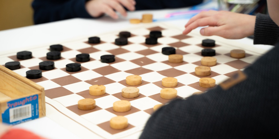 Tijdens de Denksportclub zijn kinderen een potje aan het dammen